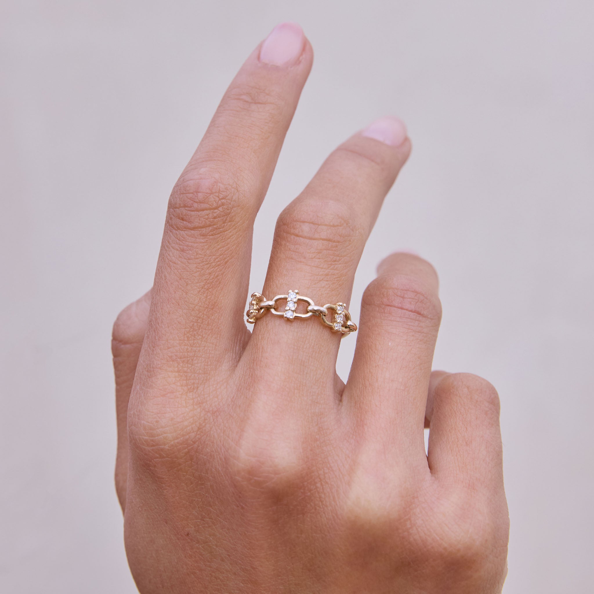 Hand wearing Zoe Chicco 14k gold open link chain ring with prong set white diamonds against a neutral background