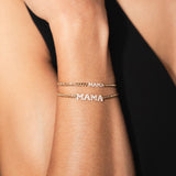 A woman wears two MAMA bracelets on small curb chain: itty bitty mama and regular block letter bracelet.