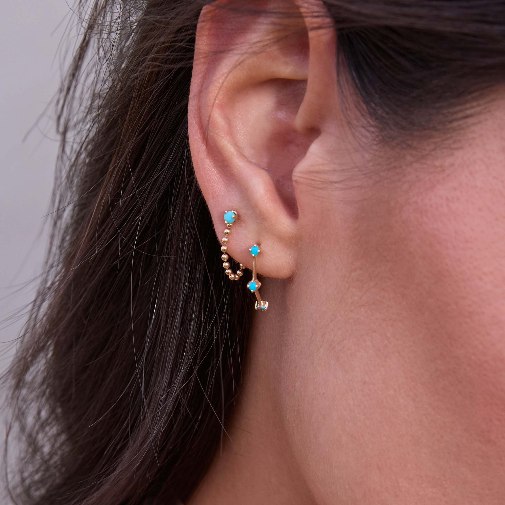 Close up of a woman with dark hair wearing Zoe Chicco 14k Prong Turquoise Bead Chain Huggie Earrings