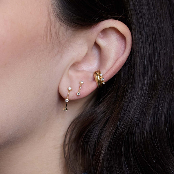 Zoe Chicco 14K  Close-up of an ear wearing gold hoop earrings with small gemstones.