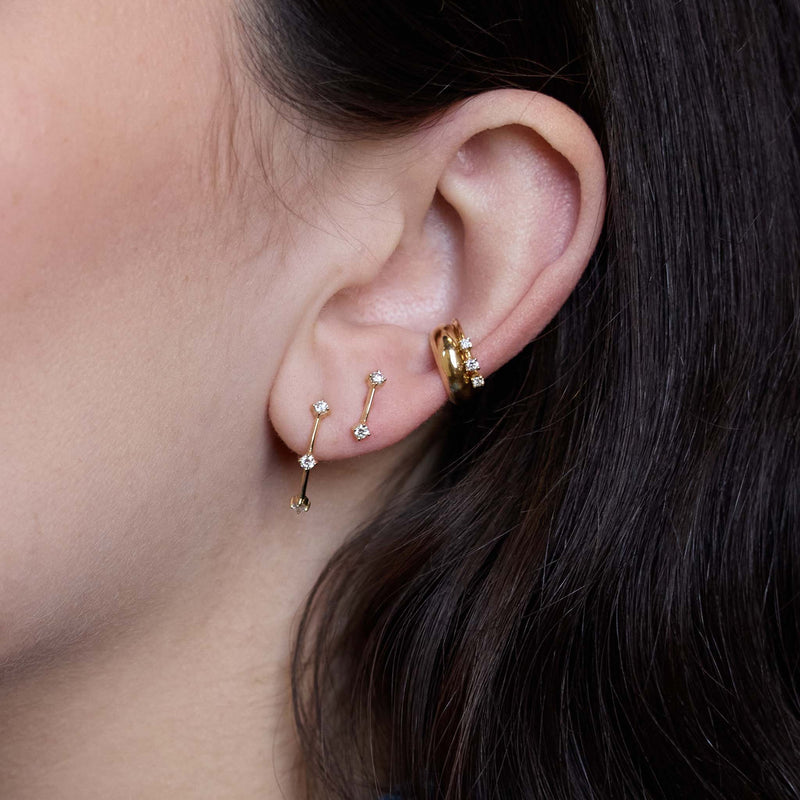 Zoe Chicco 14K  Close-up of an ear wearing gold hoop earrings with small gemstones.
