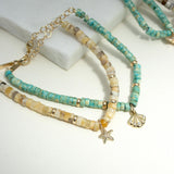 14k Gold & Sandy Feldspar Mixed Heishi Bead Starfish Charm Bracelet and 14k Gold & Light Turquoise Heishi Bead Seashell Charm Bracelet laying flat against a white background