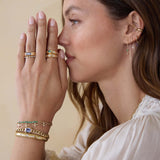 Woman wearing Zoe Chicco 14k gold jewelry including rings, bracelets, and earrings with diamonds and sapphires on a beige background