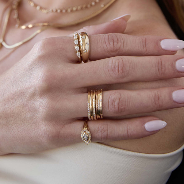 woman's hand wearing a Zoë Chicco 14k Gold Pavé Diamond Twisted Square Band Ring stacked with a 2mm Rounded Band Ring, 1.5mm Rounded Band Ring, and a 14k 12 Spread Out Diamond Band Ring on her ring finger along with a 14k Marquise Diamond Halo Signet Ring on her pinky and a 14k Scattered Star Set Diamonds Small Aura Ring and 5 Pear Diamond Ring stacked on her index finger