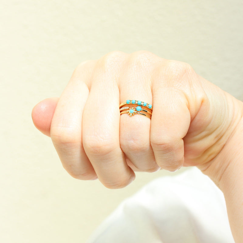 a woman's hand wearing a Zoë Chicco 14k Gold 5 Prong Turquoise Band Ring stacked with two turquoise rings on her ring finger