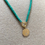 a Zoë Chicco 14k Gold Turquoise Rondelle Bead Round Enhancer Necklace laying flat against a beige background with a Medium Octagonal Mantra Pendant with "You are my sunshine" engraved on it and a pavé diamond sun