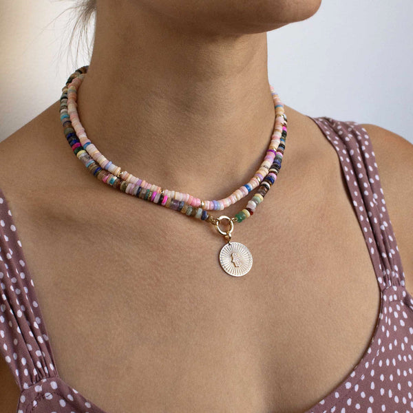 woman in a polka dot top wearing a Zoë Chicco 14k Gold & Mixed Pink Opal Rondelle Bead Necklace layered with a 14k Mixed Dark Gemstone Rondelle Bead Round Enhancer Necklace with a Pavé Diamond Hamsa Sunbeam Medallion Clip On Pendant hanging from the enhancer