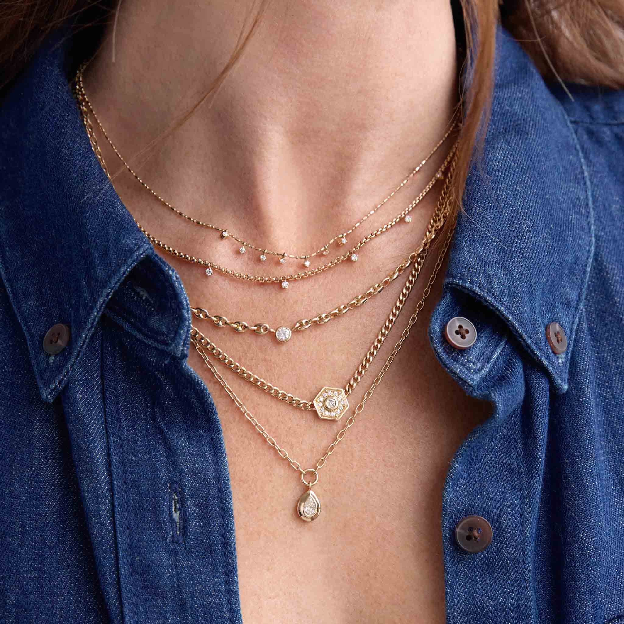close up of a woman in a denim shirt wearing a Zoë Chicco 14k Gold Floating Diamond Small Puffed Mariner Chain Necklace layered with a 14k 7 Dangling Prong Diamond Tube Bar Chain Necklace, 14k 9 Prong Diamond Small Box Chain Necklace, and a Zoë Chicco 14k Gold Small Curb Chain Diamond Hexagon Halo Necklace