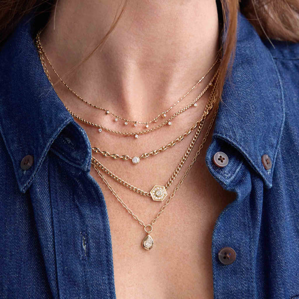 close up of a woman in a denim shirt wearing a Zoë Chicco 14k Gold Floating Diamond Small Puffed Mariner Chain Necklace layered with a 14k 7 Dangling Prong Diamond Tube Bar Chain Necklace, 14k 9 Prong Diamond Small Box Chain Necklace, and a Zoë Chicco 14k Gold Small Curb Chain Diamond Hexagon Halo Necklace