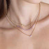 a woman wearing a Zoë Chicco 14k Gold Emerald Cut Pink Sapphire Bezel XS Curb Chain Necklace layered with a 14k Pink Sapphire Tennis Segment Small Curb Chain Necklace and a 14k 7 Dangling Prong Diamond Tube Bar Chain Necklace