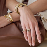 Close-up of a hand wearing gold bracelets and rings on a brown surface featuring 14k Pear Tiger Eye & Pavé Diamond Open Ring