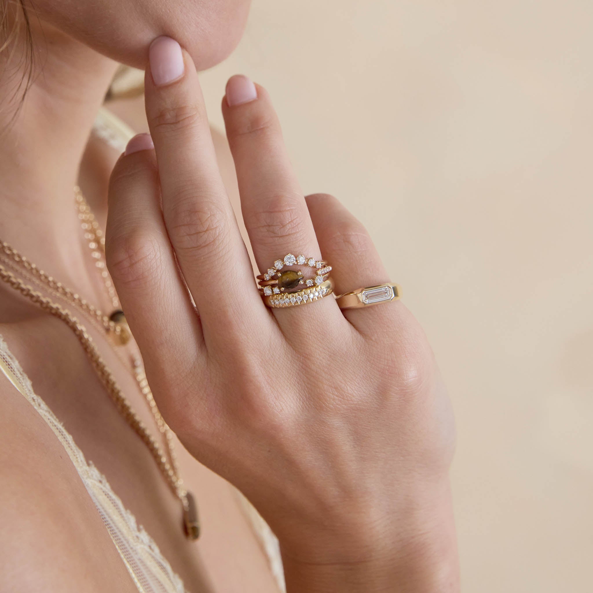 Close-up of a hand wearing multiple rings with a soft beige background featuring 14k Pear Tiger Eye & Pavé Diamond Open Ring