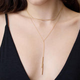 Zoe Chicco 14k gold necklace with a vertical bar pendant worn by a person in a black top.