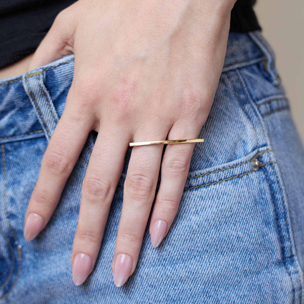 Close-up of a hand wearing a Zoe Chicco 14k gold bar ring on a denim background