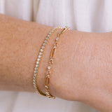 A woman's wrist wearing a Zoë Chicco 14k Gold 1.5mm Diamond Bezel Tennis Bracelet layered with a 14k Linked Prong Diamond & Medium Paperclip Rolo Chain Bracelet