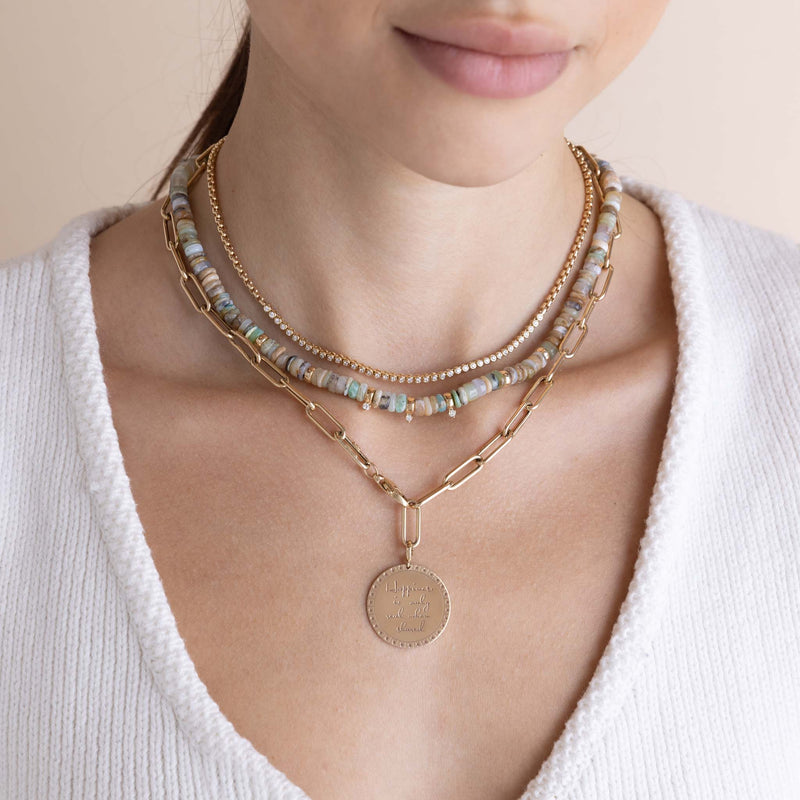 woman in a white sweater wearing a Zoë Chicco 14k Gold Mixed Neutral Gemstone Rondelle Bead Necklace with 3 Prong Diamonds layered with a 14k Small Diamond Bezel Tennis Segment Box Chain Necklace and a Large Paperclip Chain Lariat with a Large Mantra Disc Charm clipped on