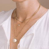 woman wearing a Zoë Chicco 14k Gold .28 ctw Shield Diamond Bezel Necklace layered with a 14k Small Diamond Bezel Tennis Segment Box Chain Necklace and a 14k Gold Custom Names Star Set Round Locket Necklace