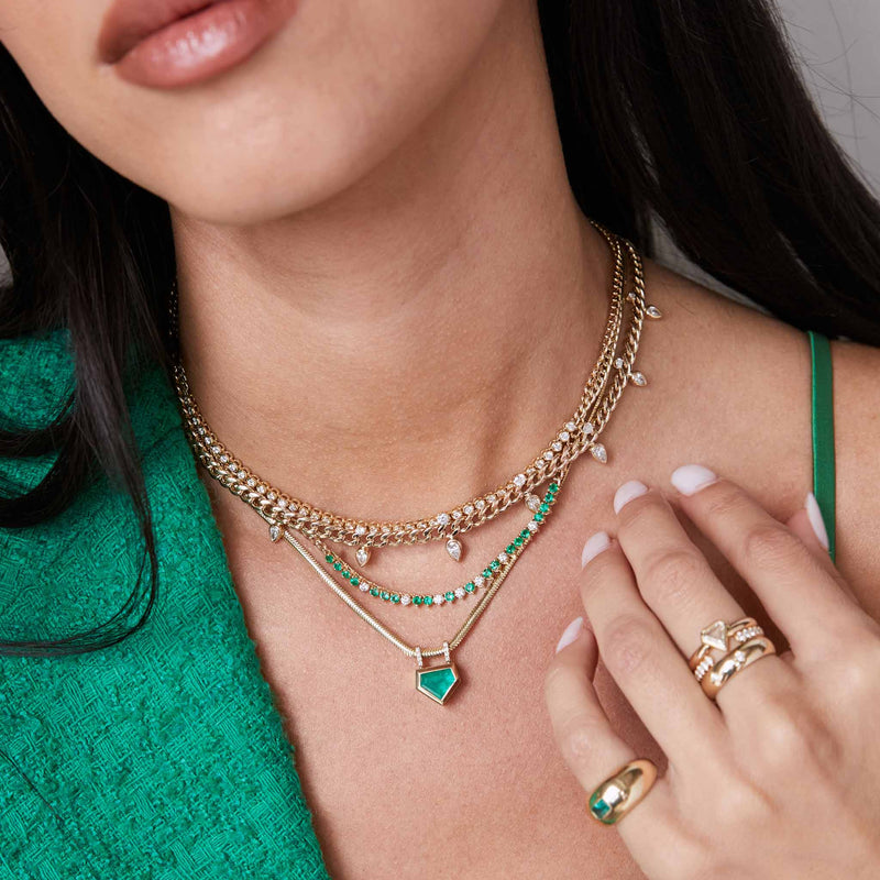 woman in a green jacket wearing a Zoë Chicco 14k Gold Graduated Stacked Pear & Round Diamond Medium Curb Chain Necklace with three other diamond and emerald necklaces