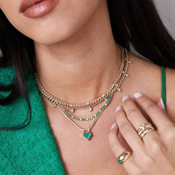 a woman wearing a green top and a Zoë Chicco 14k Gold One of a Kind Shield Emerald Bezel Snake Chain Necklace layered with three other necklaces