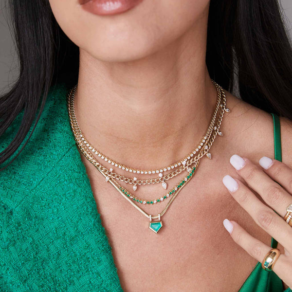 a woman in a green top wearing a Zoë Chicco 14k Gold 3" Diamond Bezel Tennis Segment Small Curb Chain Necklace layered with three other necklaces