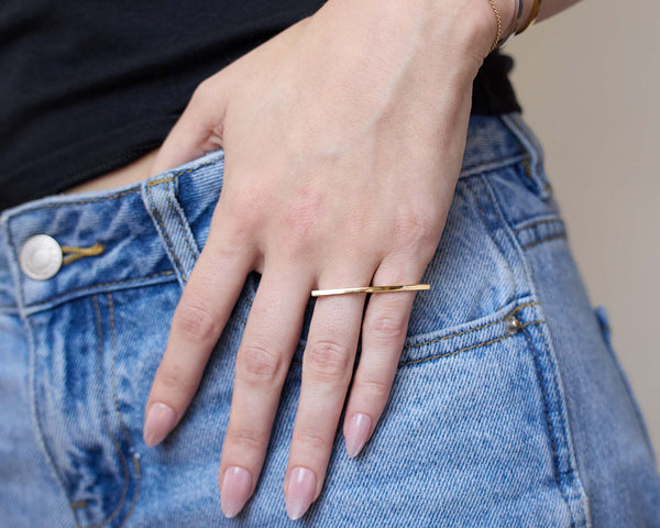 Close-up of a hand wearing a Zoe Chicco 14k gold bar double finger ring on a denim background
