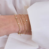 woman in a white shirt wearing a Zoë Chicco 14k Gold Pear Diamond XS Curb Chain Bracelet layered with a 14k Linked Prong Diamond & Medium Paperclip Rolo Chain Bracelet, 14k Princess Diamond & Diamond Bar Bracelet, and a Baguette Diamond Curb Chain Bracelet, and a 14k 5 Vertical Baguette Diamond Station Small Curb Chain Bracelet