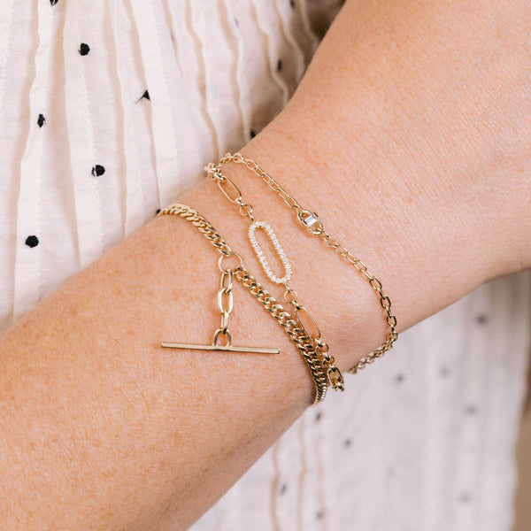a woman in a dotted shirt wearing a Zoë Chicco 14k Gold Single Pavé Diamond Link Medium Paperclip Rolo Chain Bracelet on her wrist layered with a Baguette Diamond Open Link Bracelet and a 14k Mixed Small Curb & Medium Square Oval Chain Toggle Bracelet