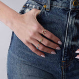 woman's hand resting against jeans wearing a Zoë Chicco 14k Gold Emerald Cut Ruby Bezel Pavé Diamond Band Ring stacked with a 14k Tapered Baguette & Prong Diamond Curved Bar Ring on her index finger, a 14k Emerald Cut Blue Sapphire Diamond Halo Signet Ring on her middle finger, and 14k Pear Turquoise & Pavé Diamond Open Ring and a 14k Prong Turquoise & Pavé Diamond Open Ring on her ring finger