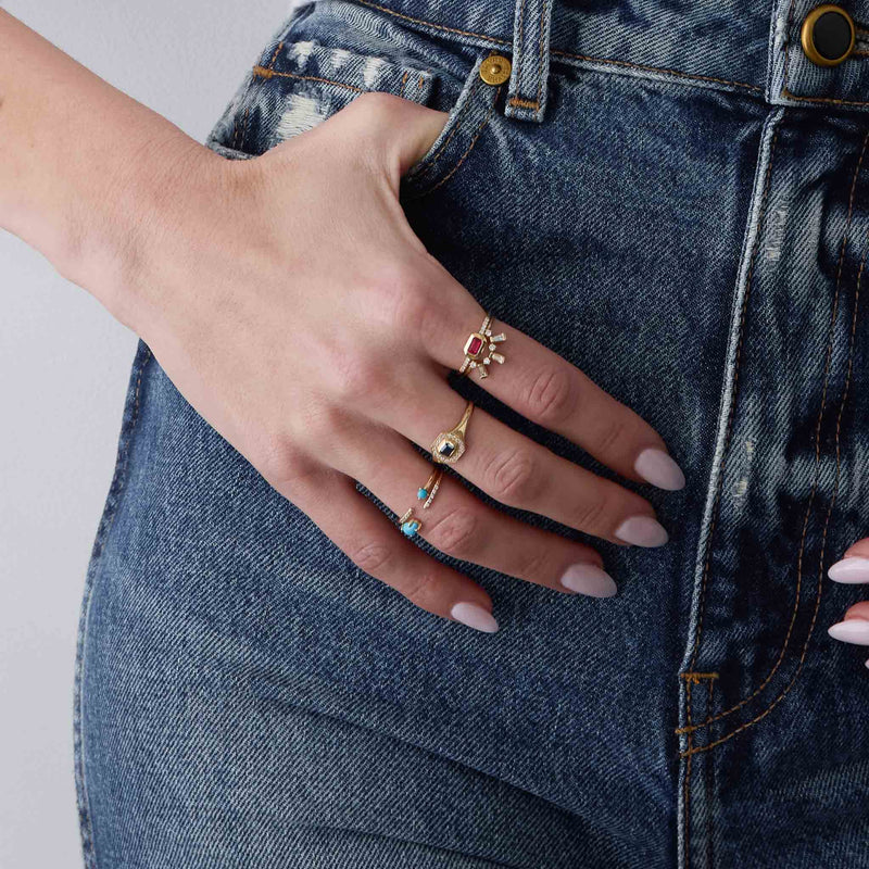 woman's hand resting against jeans wearing a Zoë Chicco 14k Gold Emerald Cut Ruby Bezel Pavé Diamond Band Ring stacked with a 14k Tapered Baguette & Prong Diamond Curved Bar Ring on her index finger, a 14k Emerald Cut Blue Sapphire Diamond Halo Signet Ring on her middle finger, and 14k Pear Turquoise & Pavé Diamond Open Ring and a 14k Prong Turquoise & Pavé Diamond Open Ring on her ring finger