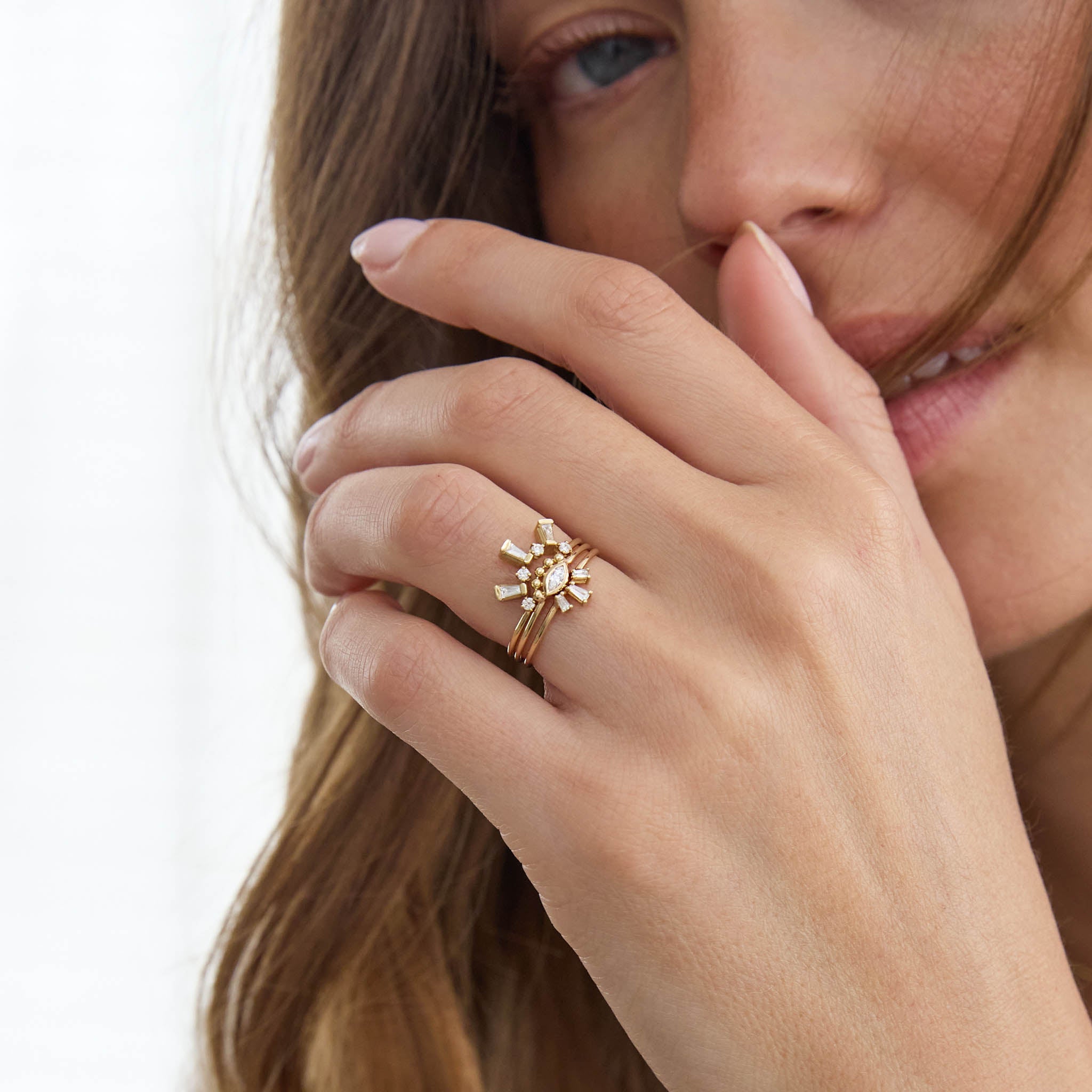 Close-up of a hand wearing Zoe Chicco 14k gold rings with diamonds creating a starburst design, touching the face.