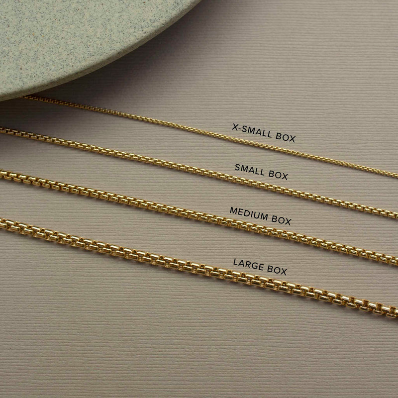An image of four Zoë Chicco 14k Gold Box Chain Necklaces laid flat on a brown background comparing four different sizes  (extra small, small, medium, and large)