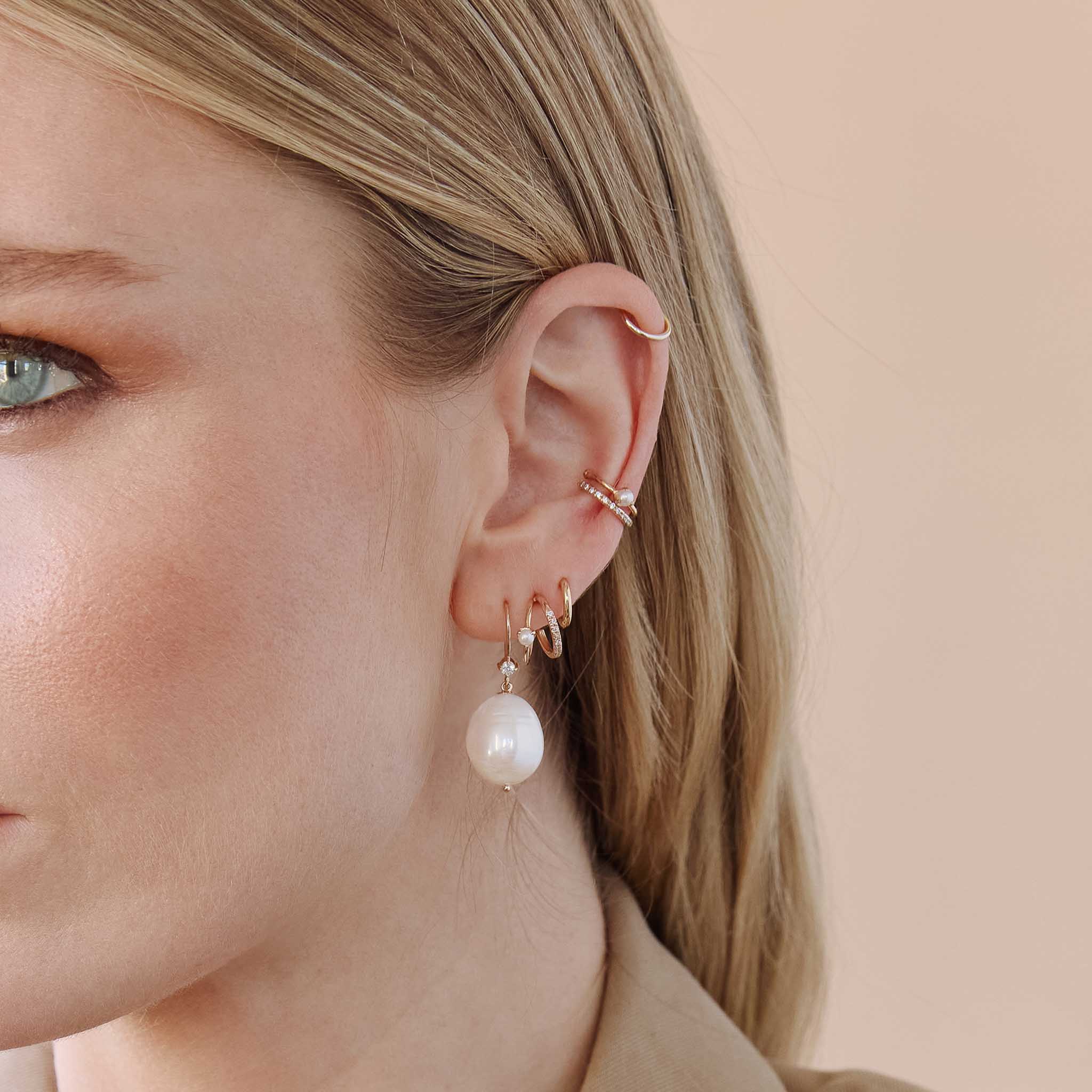close up of a woman's ear wearing a Zoë Chicco 14k Gold Pearl & Pavé Diamond Angled Double Wire Huggie Hoop Earring in her second piercing layered with a 14k Prong Diamond & Baroque Pearl Wire Earring, XS huggie hoop, 14k Prong Set Pearl Ear Cuff, and a Thick Pave Diamond Ear Cuff