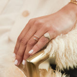 close up of a woman's hand resting on the edge of a chair wearing a Zoë Chicco 14k Gold Full Pavé Diamond Oval Signet Ring on her pinky finger and a Zoë Chicco 14k Gold Pavé & Marquise Diamond Bypass Ring on her ring finger