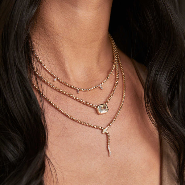 a close up of a brunette woman wearing a Zoë Chicco 14k Gold 5 Vertical Baguette Diamond Medium Box Chain Necklace layered with a 14k Gold Pavé Diamond Serpent Box Chain Necklace and a one of a kind 3.53 ctw Emerald Cut Ombre Sapphire Box Chain Necklace