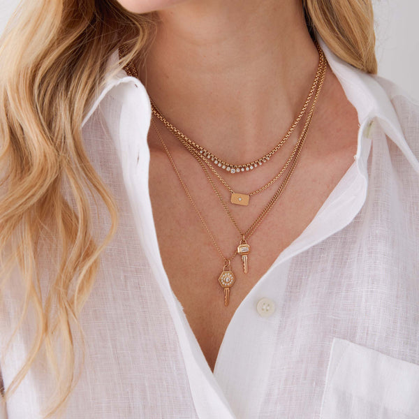 woman in a white shirt wearing a Zoe Chicco's 14k Diamond Hexagon Halo Key Pendant Necklace and 14k Emerald Cut Diamond Bezel Key Pendant Necklace layered with a 14k Graduated Prong Diamond Medium Box Chain Necklace and a 14k Horizontal Star Set Diamond Square Edge Dog Tag Necklace