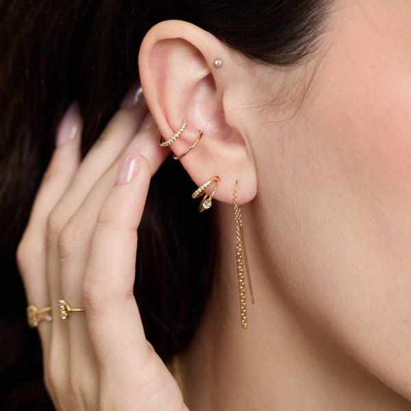 Close-up of a person wearing Zoe Chicco 14k gold earrings and rings with a blurred background
