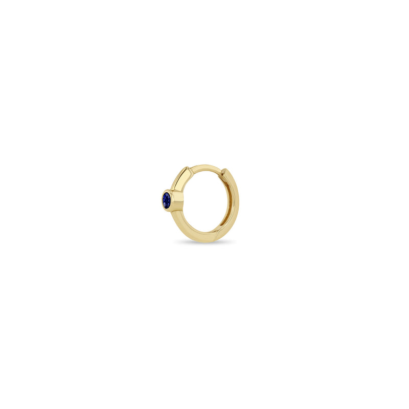 Angled view of a Zoë Chicco 14k Gold Single Blue Sapphire Bezel Small Hinge Huggie Hoop Earring