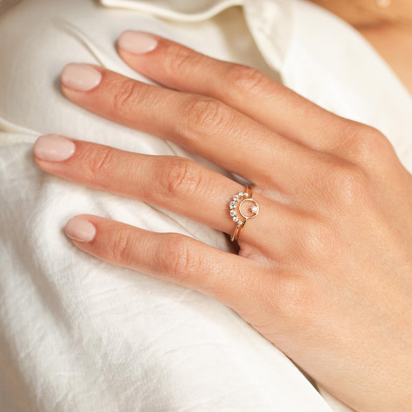 A woman in a white shirt is wearing a stack of two rings that feature prong diamonds: the small circle with diamond and the 7 diamond arc nesting ring.