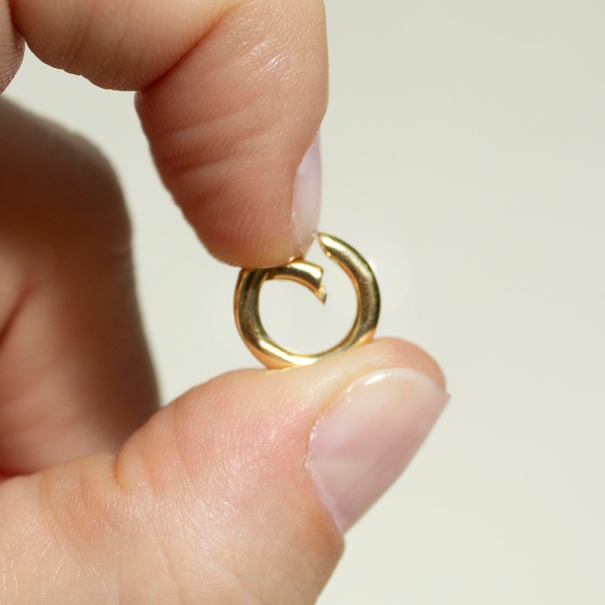 close up of a woman holding a 14k gold push lock round circle enhancer between her thumb and index finger pushing the clasp inwards