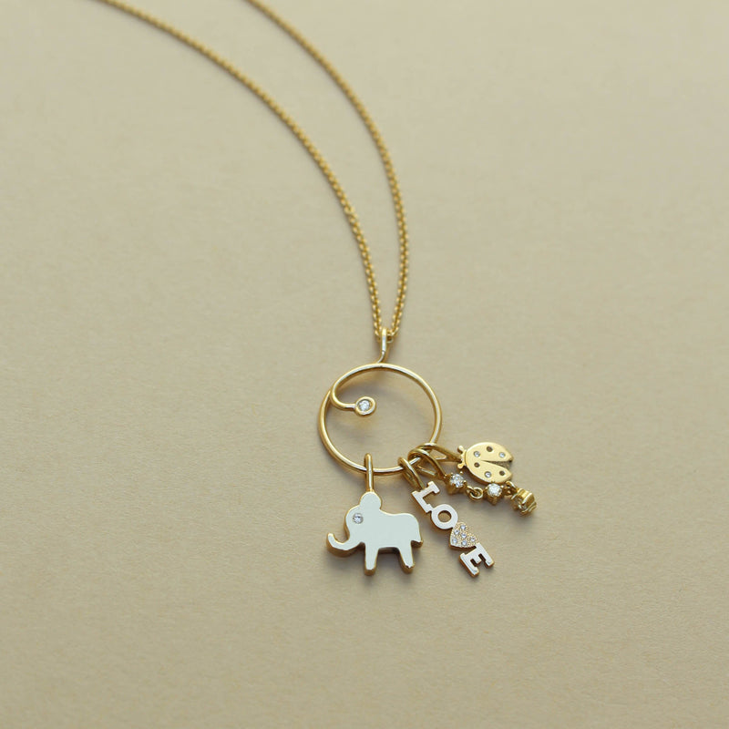 A Zoë Chicco 14k Gold Diamond Circle Charm Holder Pendant on a chain laying flat with an Elephant charm, Itty Bitty LOVE with Pavé Diamond Heart Charm, 3 Prong Diamond Drop Charm Pendant, and a Midi Bitty Diamond Ladybug Charm attached to the charm holder