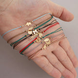 In the palm of a woman's hand, is a variety of cord bracelets with various charms and symbols. 