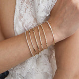 Close-up of a person's wrist wearing multiple Zoe Chicco 14k gold flex diamond tennis bangle bracelets on a light background