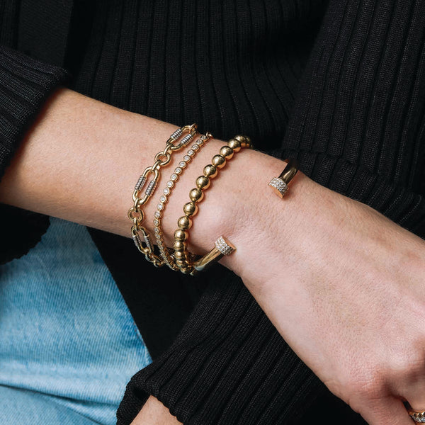 woman in a black sweater and jeans wearing a Zoë Chicco 14k Gold Ball Bead Bracelet stacked with a 2mm 14k Gold Diamond Bezel Tennis Bracelet and a 14k Pavé Diamond Door Knocker Cuff on her arm