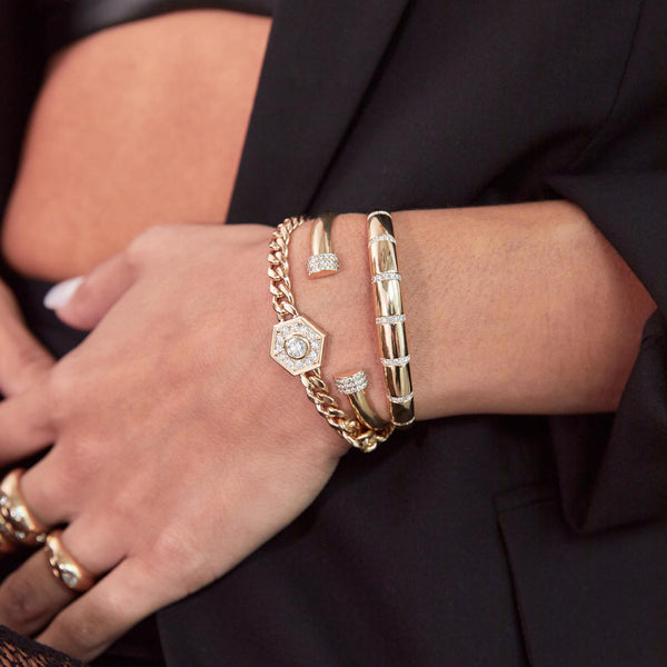 woman in a black blazer wearing a Zoë Chicco 14k Gold Pavé Diamond Banded Small Aura Cuff Bracelet on her wrist layered with two other bracelets