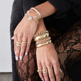 woman with her arms crossed over her lap wearing a Zoë Chicco 14k Gold Large Curb Chain Diamond Hexagon Halo Bracelet layered with two gold and diamond cuffs on her wrist