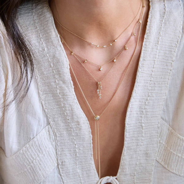 Close-up of woman wearing Zoe Chicco chain necklaces with diamonds and a round diamond box chain bolo necklace and wearing a linen shirt