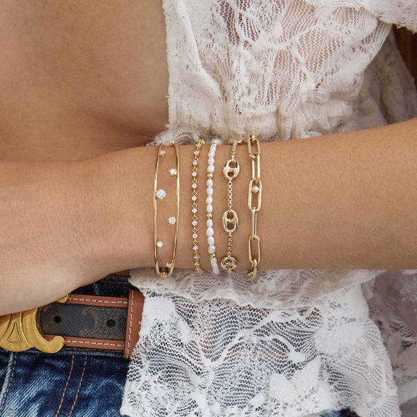 Close up of a woman's arm resting on her waist wearing a Zoë Chicco 14k Gold 5 Large Mariner Link Station Small Box Chain Bracelet stacked with a 14k Gold Bead Station Rice Pearl Bracelet, 14k Prong Diamond Double Band Cuff, 14k Linked Prong Diamond Tennis Bracelet, and a 14k Nested Pearl Large Paperclip Chain Bracelet