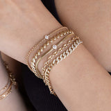 woman's wrist wearing a Zoë Chicco 14k Gold San Marco Chain Bracelet stacked with a Floating diamond Box Chain Bracelet, Floating Diamond Small Snake Chain Bracelet, Small Mariner Chain Bracelet, and a 14k Pavé Diamond Segment Medium Curb Chain Bracelet