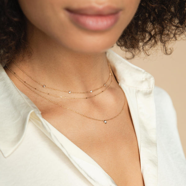 A woman wears a 5-floating diamond necklace and a double layer floating diamond with tiny bar and cable. 