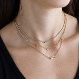 Close-up of a person wearing multiple Zoe Chicco 14k gold chain necklaces with diamonds and a single emerald